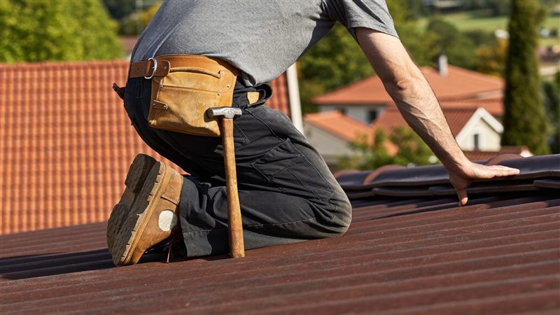 Dachdecker verlegt Ziegel auf einem Steildach, rote Dächer im Hintergrund